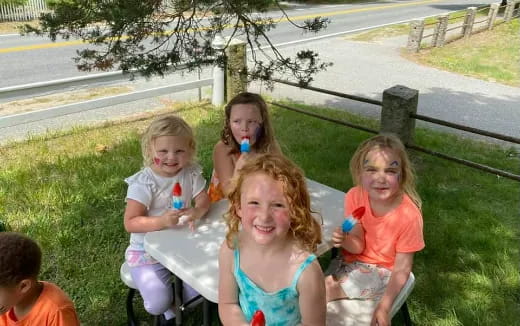 a group of children sitting on a bench in a grassy area