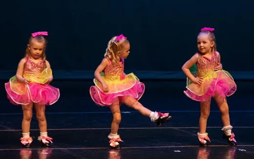 a group of girls wearing dresses and dancing on a stage