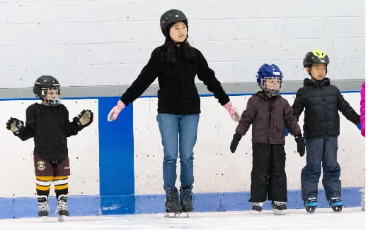 a person and several kids wearing helmets and ice skates