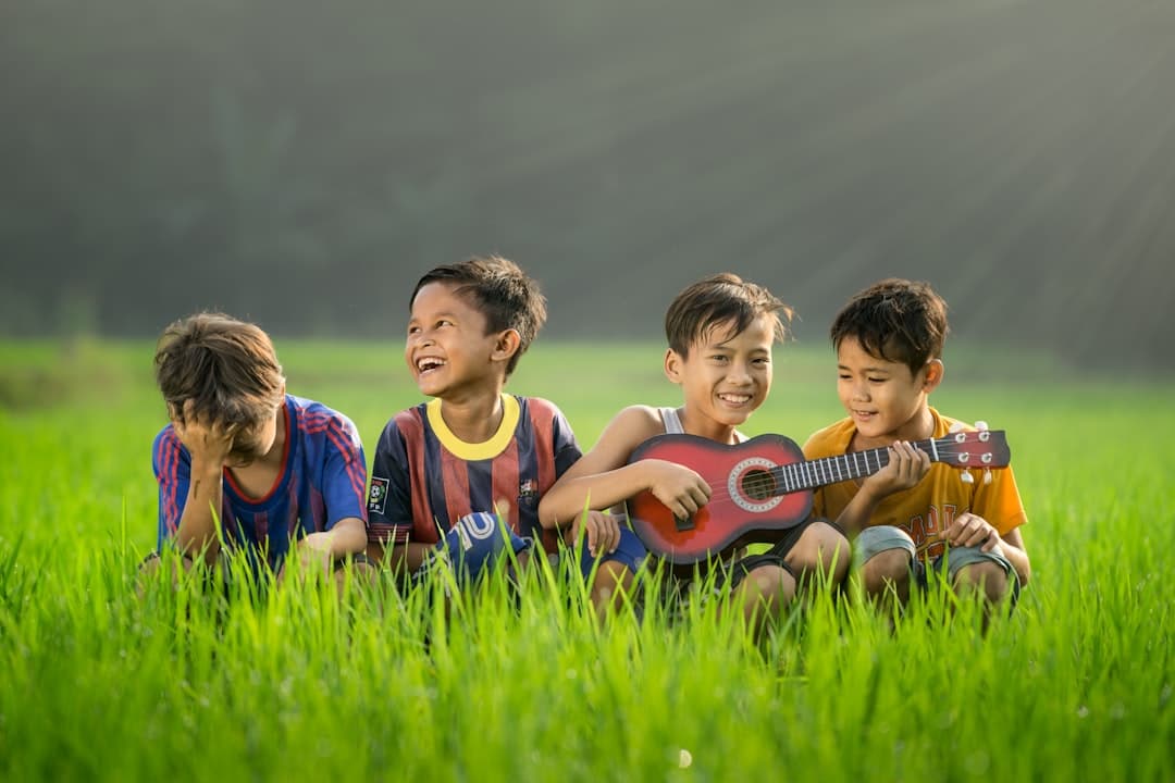 four boys laughing and sitting on grass during daytime