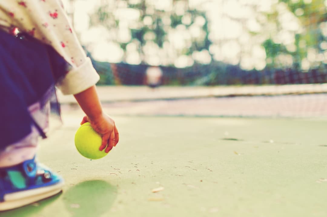 kid holding tennis ball in front of goal net