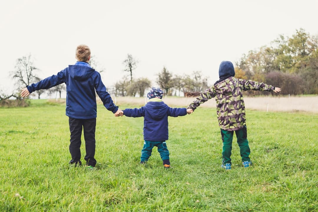 three children holding hands standing on grasses