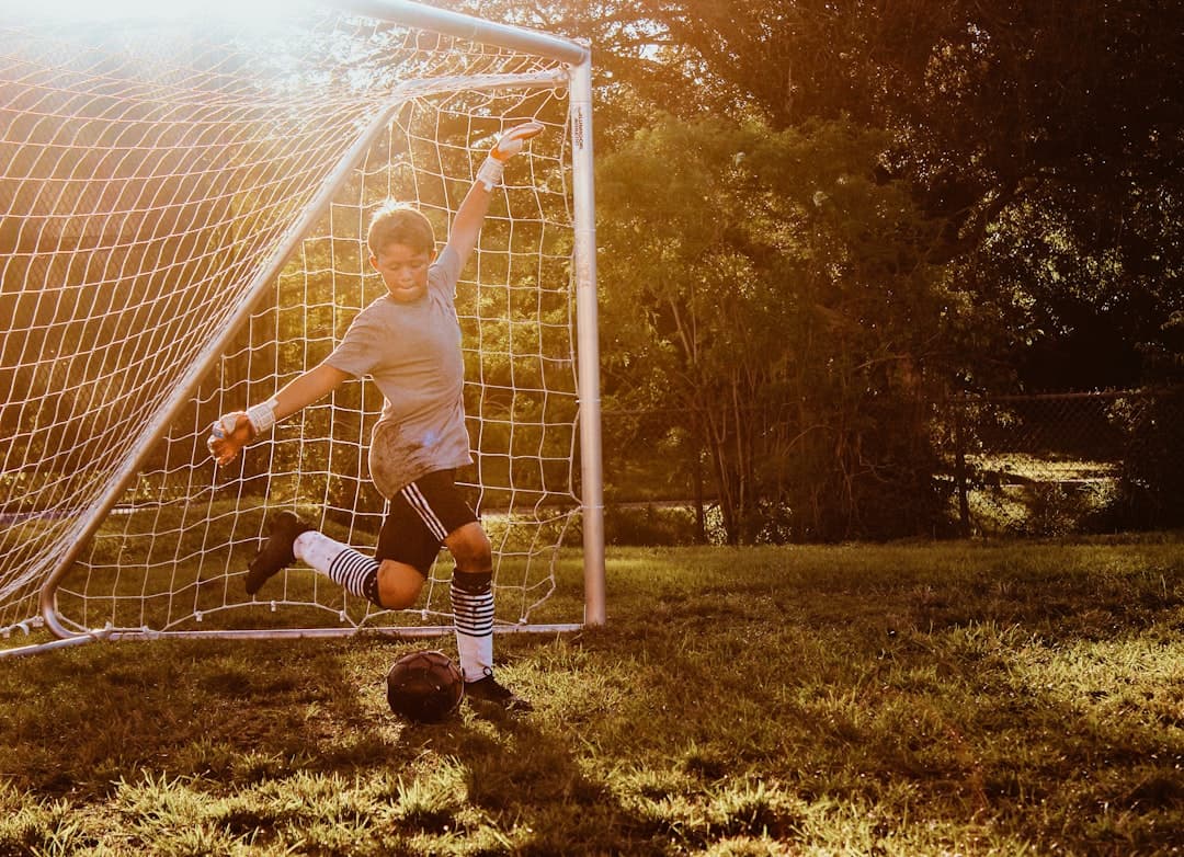boy kicking black soccer ball beside soccer goal