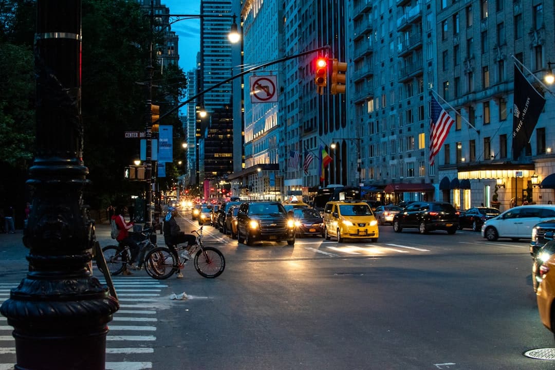 people walking on pathway near city buildings and different vehicles on road during night time