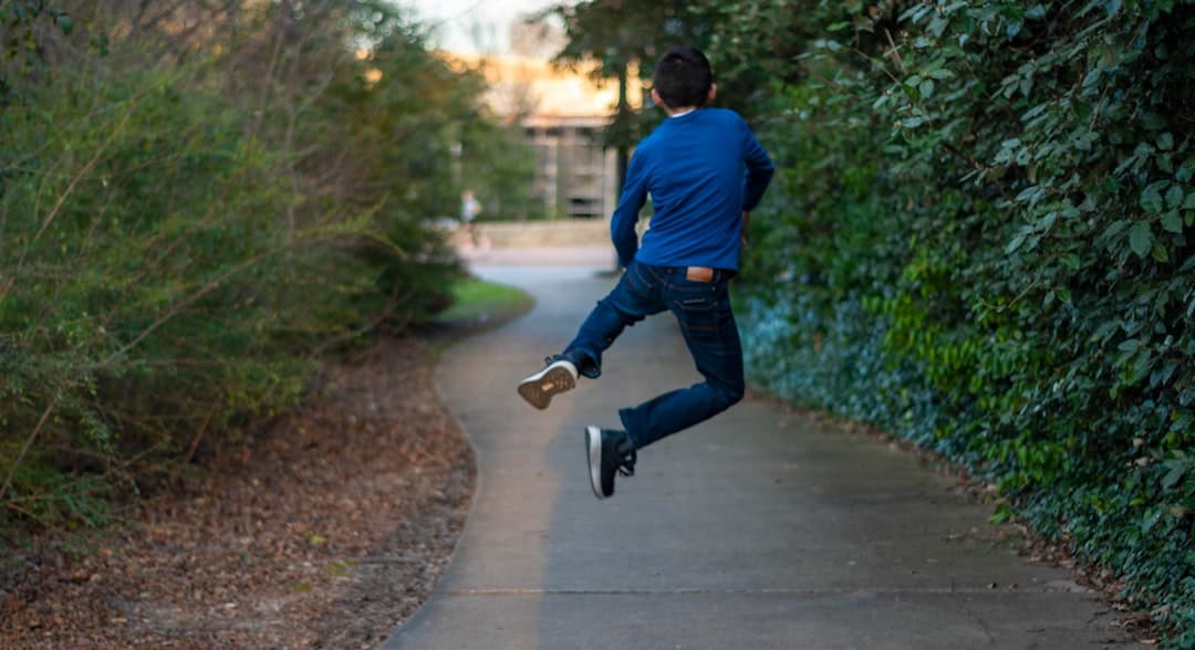 man in blue long sleeve shirt and blue denim jeans walking on gray concrete pathway during