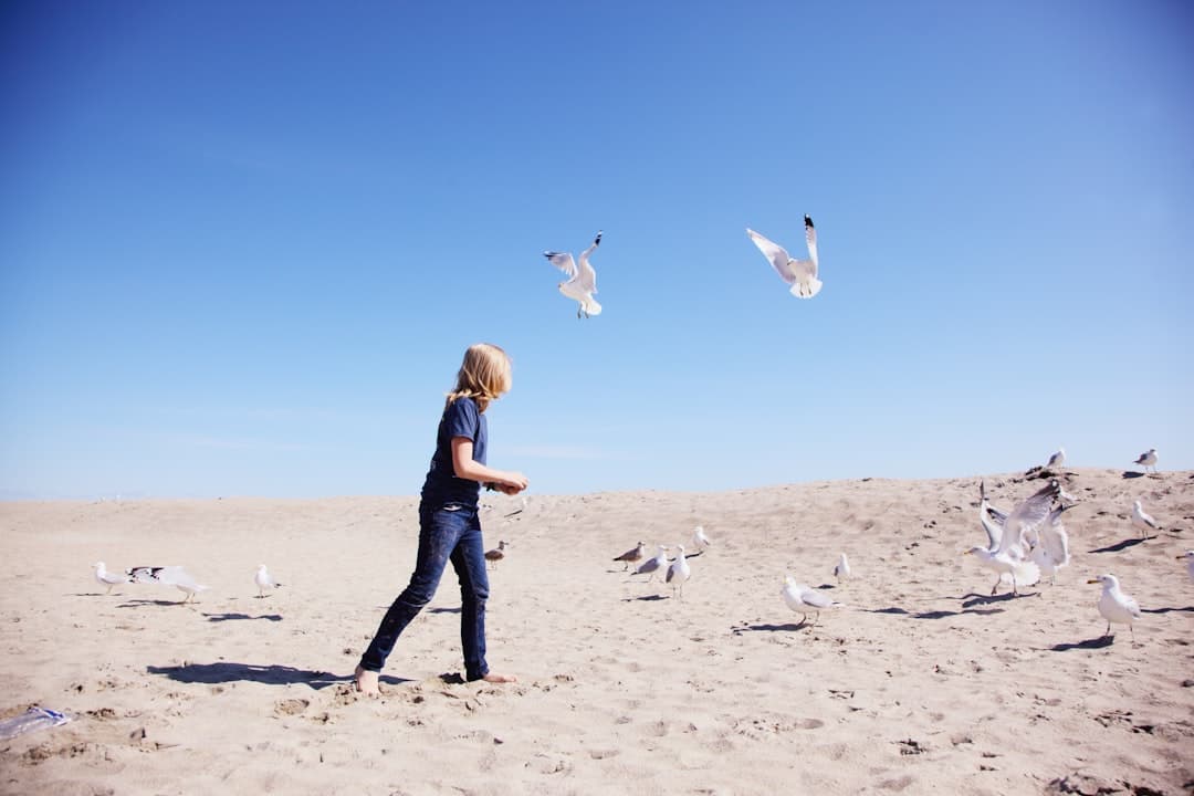 woman in blue denim jeans and white long sleeve shirt standing on white sand during daytime