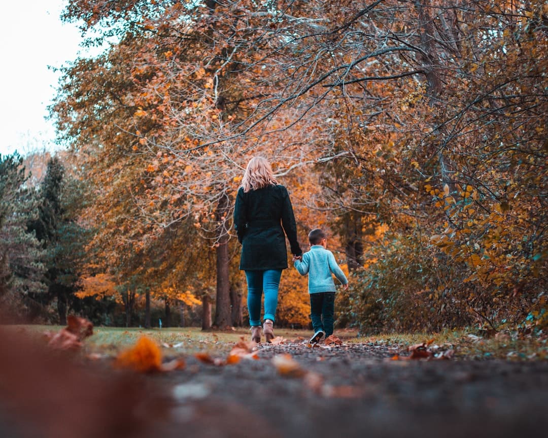 woman in black jacket and blue denim jeans walking on dried leaves on ground with brown