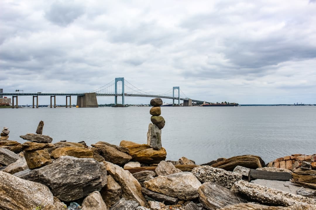 woman in brown jacket standing on brown rock near body of water during daytime