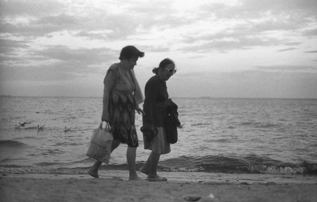 grayscale photo of couple walking on beach