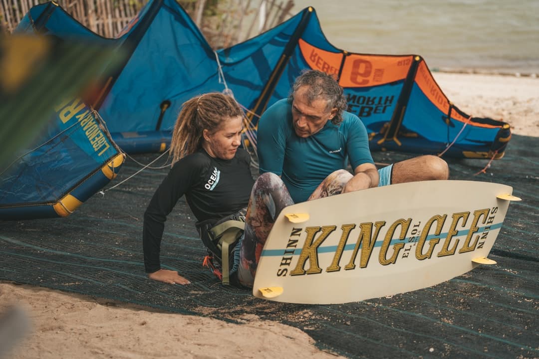 a man and a woman sitting on a beach next to a surfboard