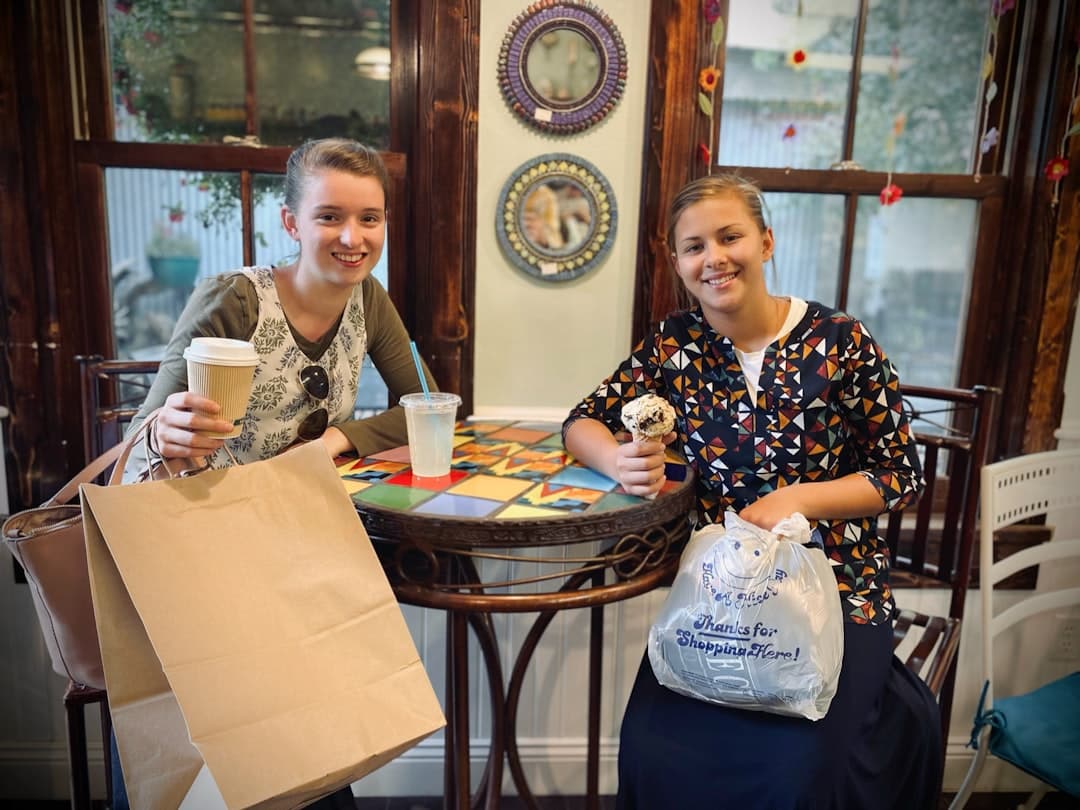 a couple of women sitting at a table with paper bags