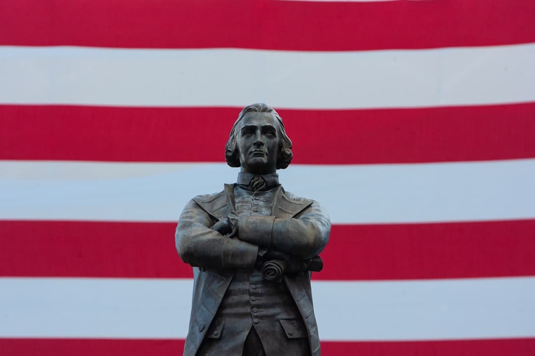 a statue of a man standing in front of a large american flag