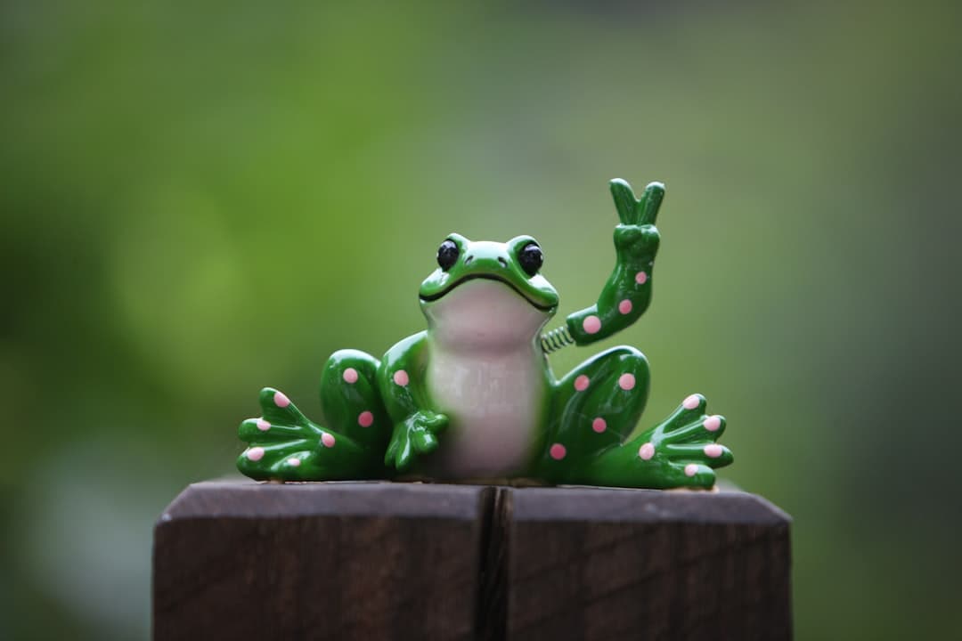 a green frog sitting on top of a wooden fence