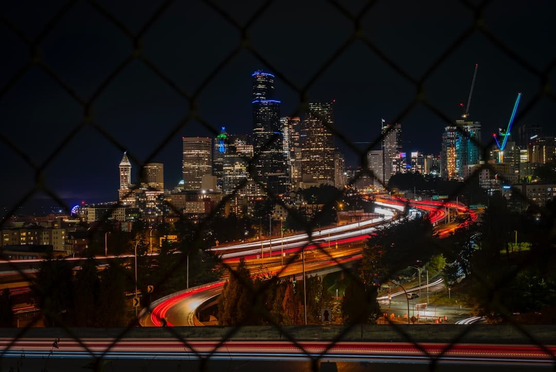 a view of a city at night through a chain link fence